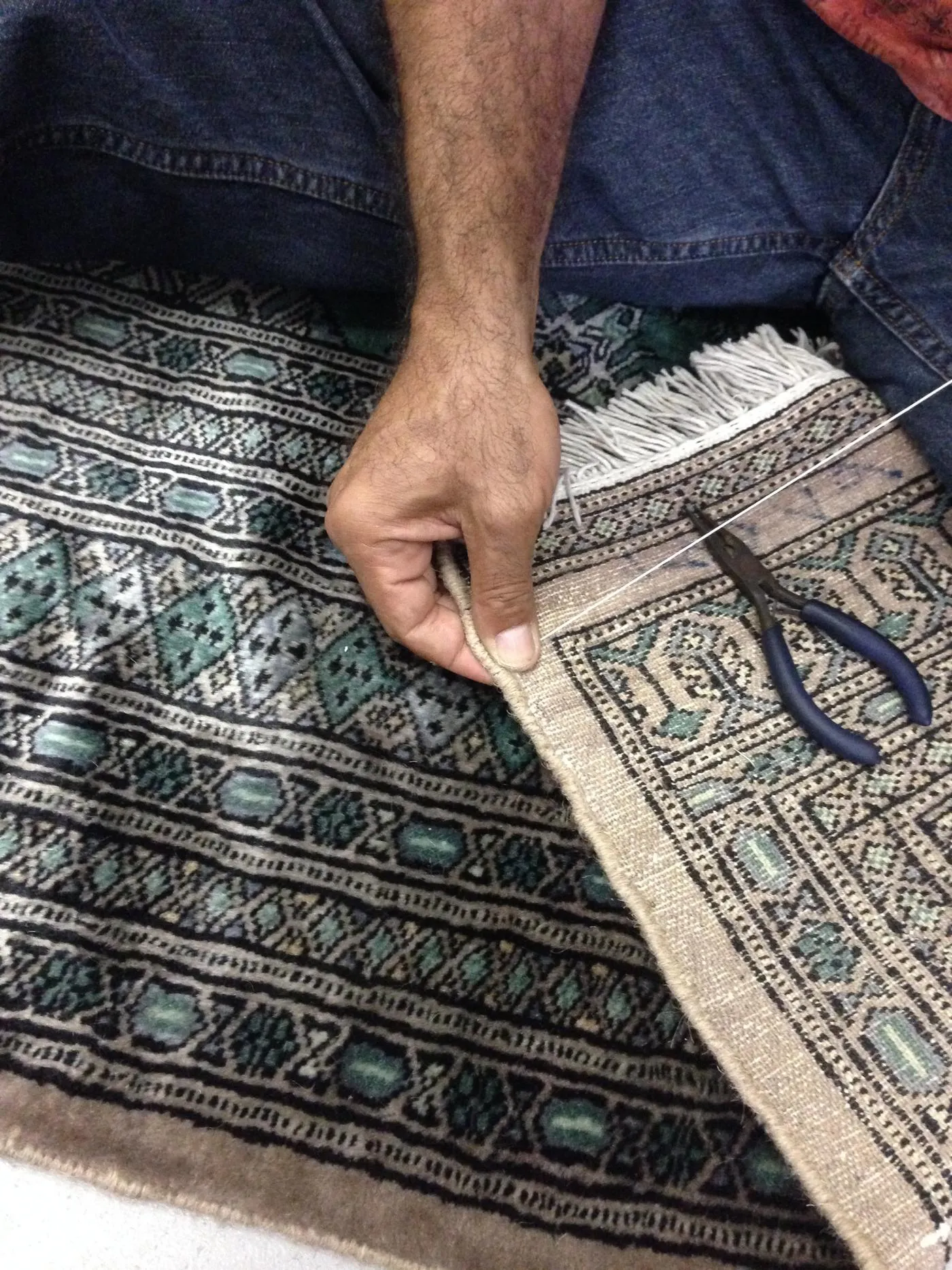 Repairer working an edge by hand with needle and pliers on the rug's back