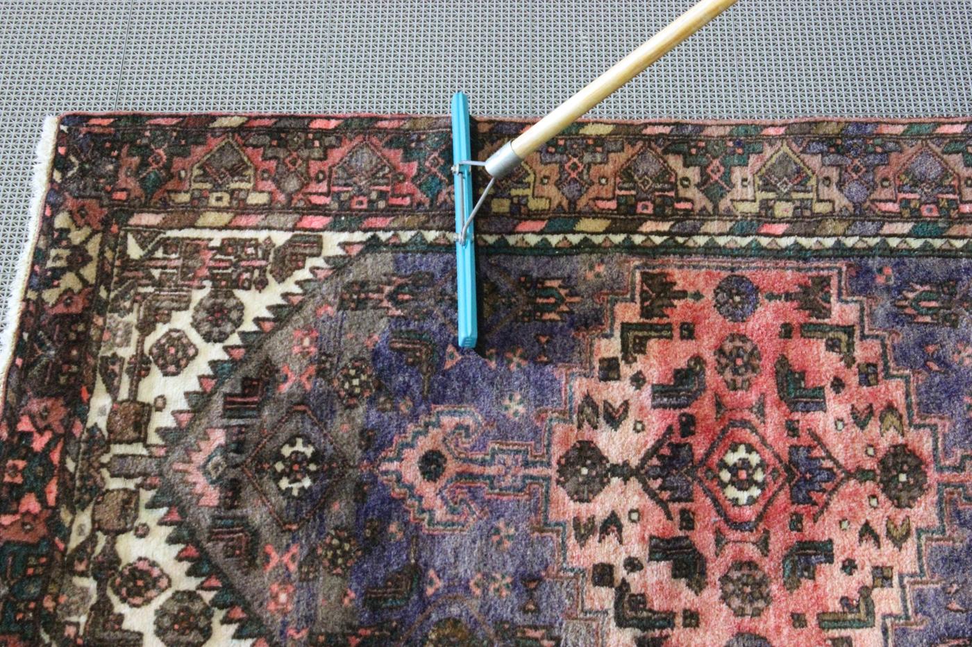 Pile brush being drawn across a hand-knotted rug to finish the nap