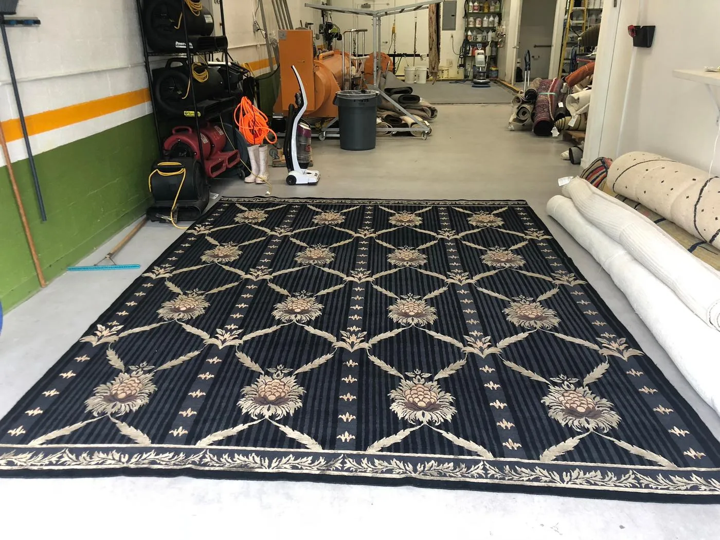 Inside the Weston rug shop: a large rug laid out for inspection with rolled rugs and drying equipment