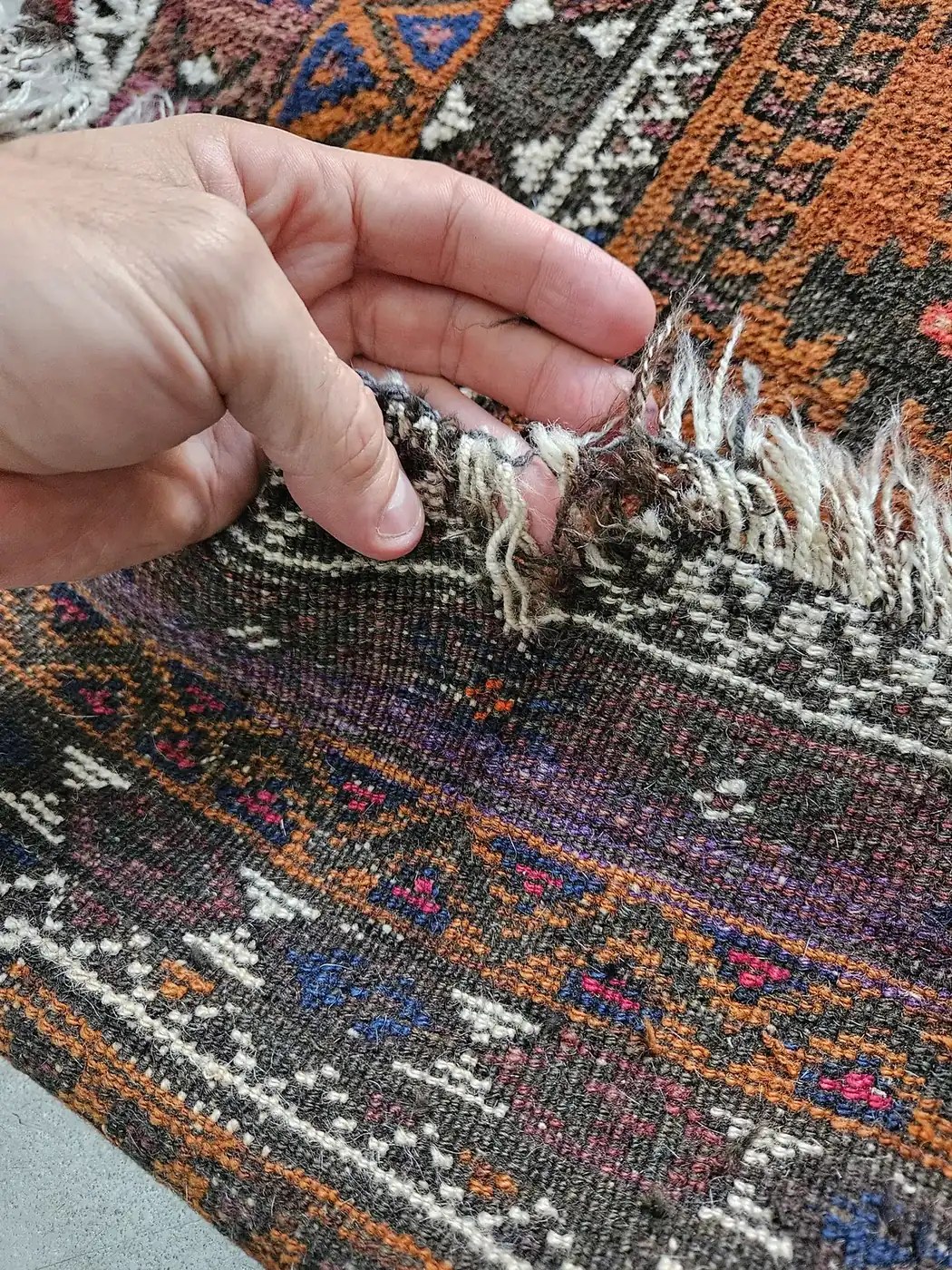 Hand lifting loose fringe on a colourful tribal rug