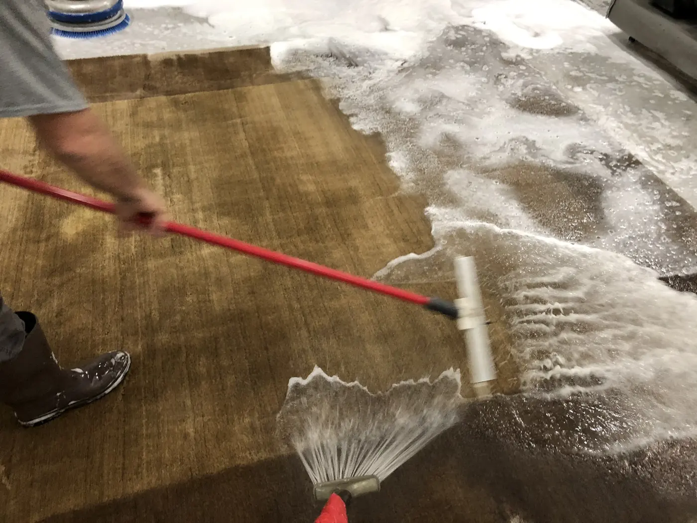 Technician rinsing a rug with a wand on the wash floor