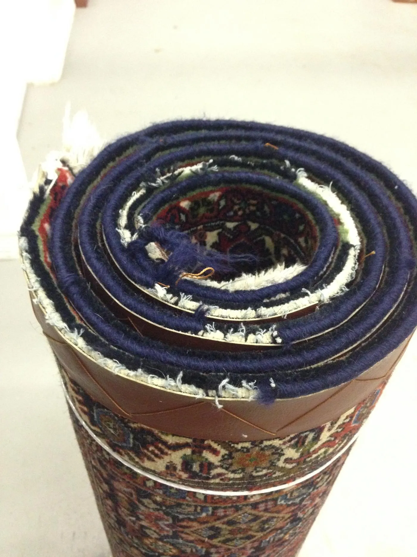 Rolled rug showing a worn end with exposed foundation awaiting repair