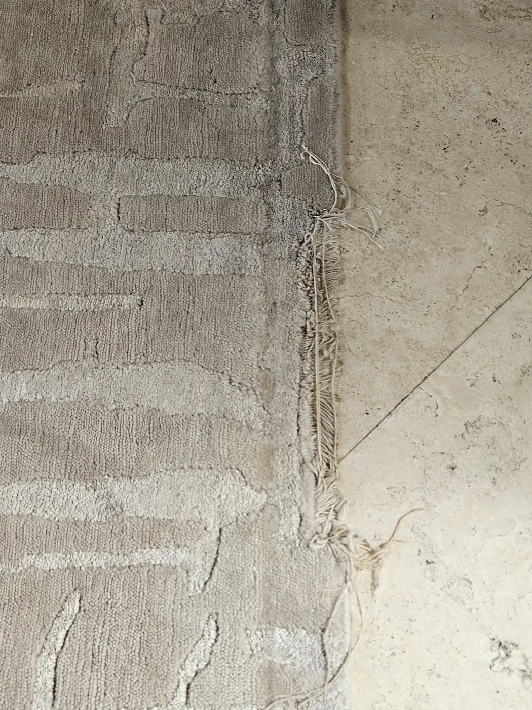 Worn end of a pale rug with the foundation threads exposed